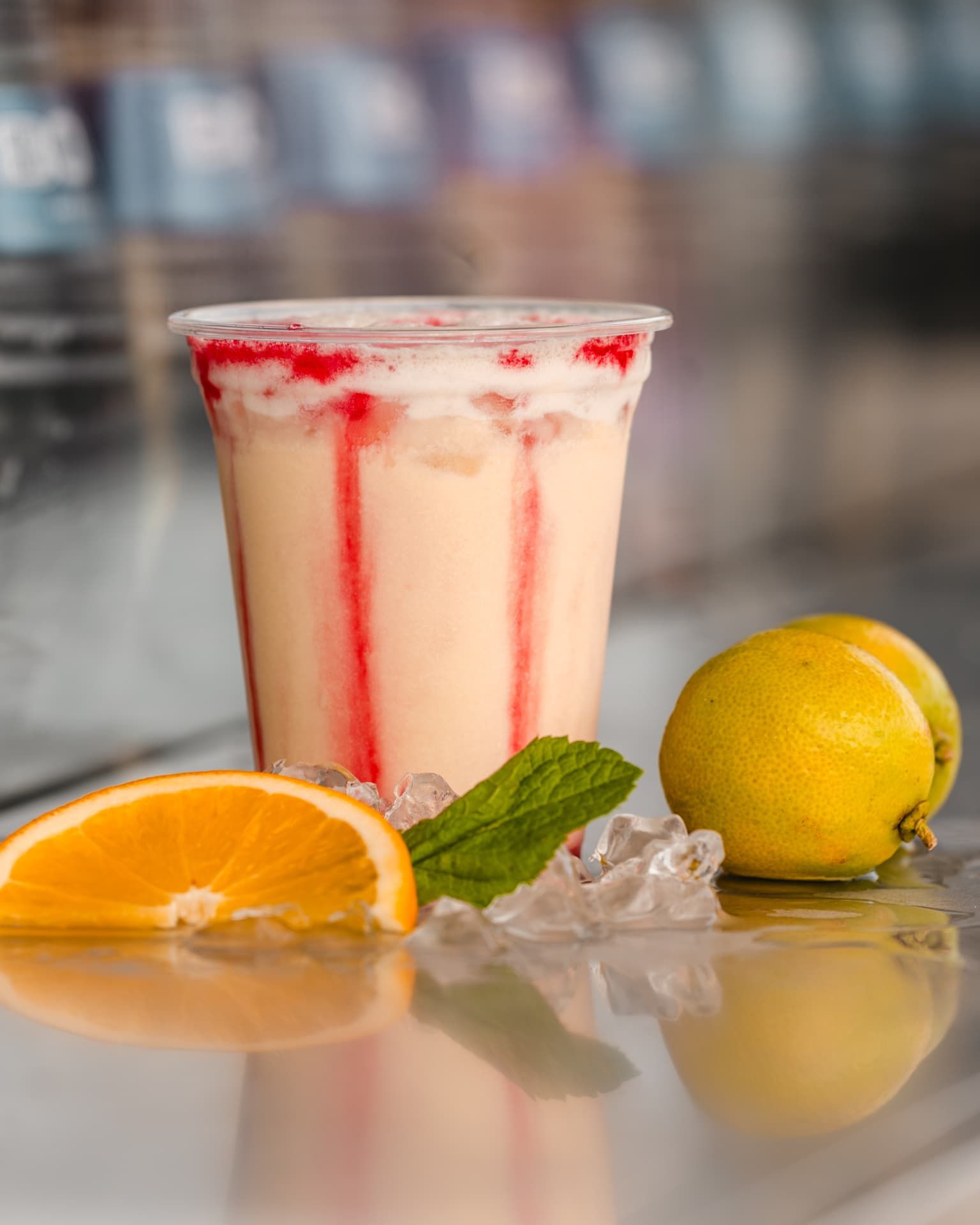 Cremiger Cocktail mit Grenadine-Schlieren, Orange, Minze und Limette auf Eis